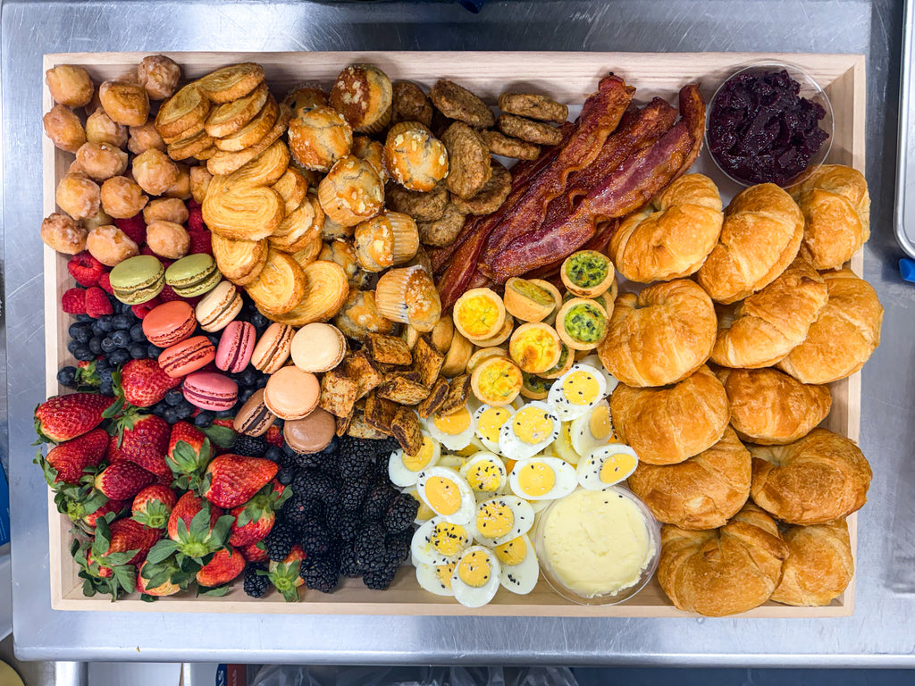 Breakfast platter with hard boiled eggs, bacon, sweet treats, fruit, croissants, butter and macaroons. 