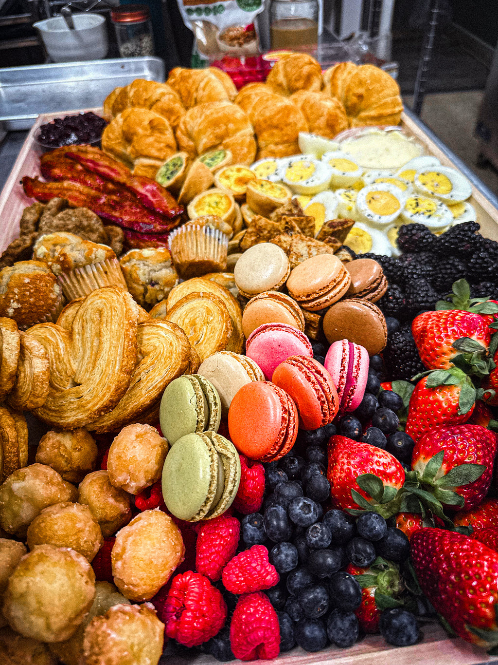 Breakfast platter with hard boiled eggs, bacon, sweet treats, fruit, croissants, butter and macaroons. 