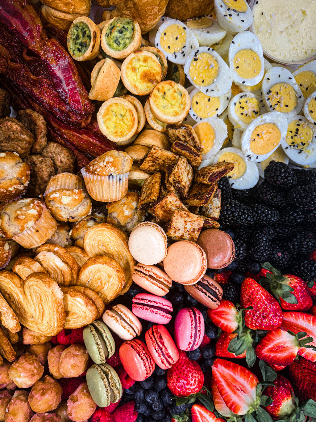 Breakfast platter with hard boiled eggs, bacon, sweet treats, fruit, croissants, butter and macaroons. 