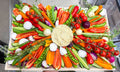 Colorful vegetable platter with hummus in the center on a kitchen counter.
