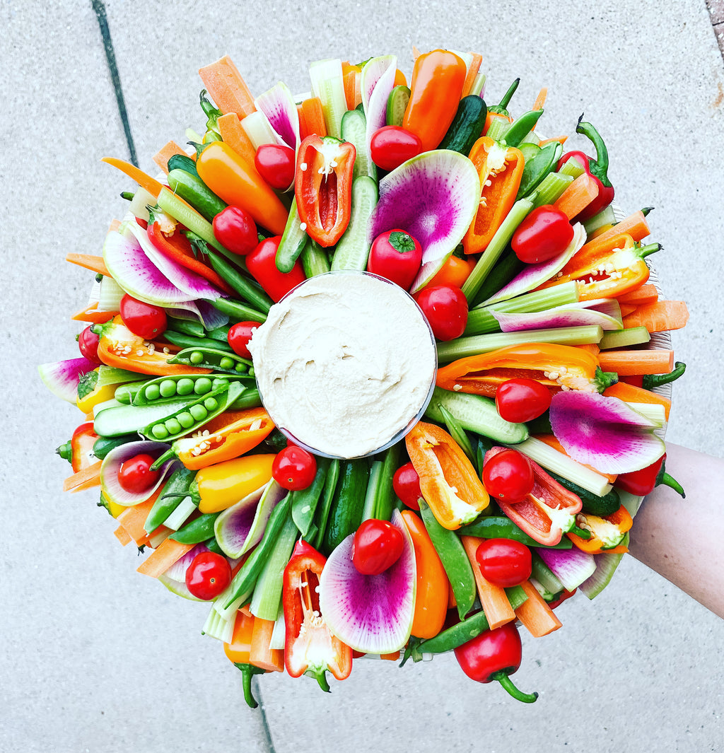 Colorful vegetable wreath with a bowl of dip in the center on a light gray background