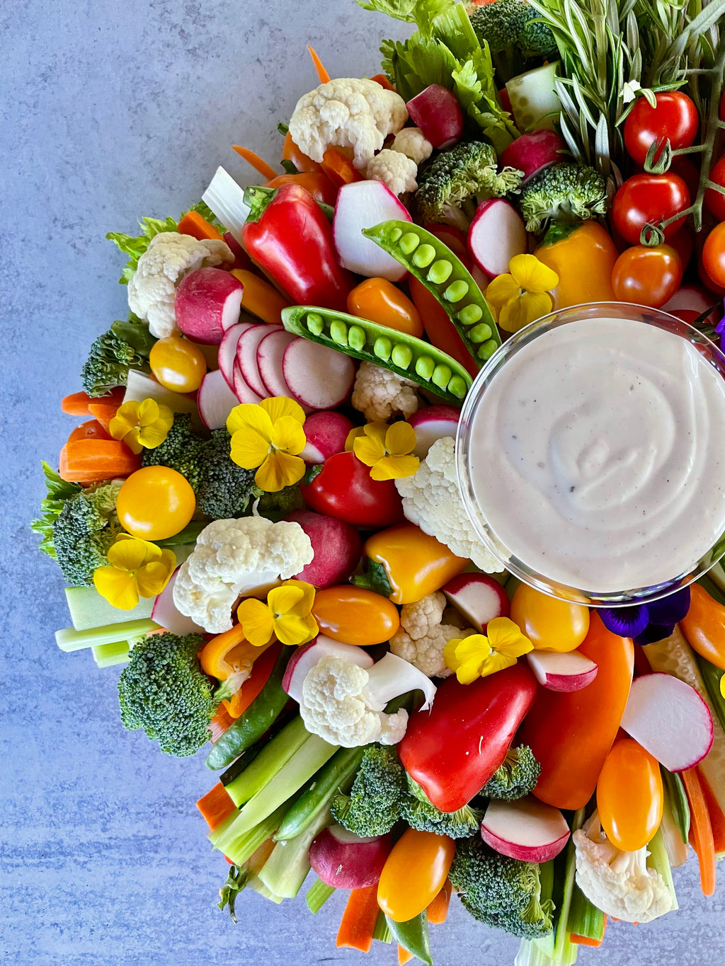 Assorted vegetables arranged with a bowl of hummus on a blue background